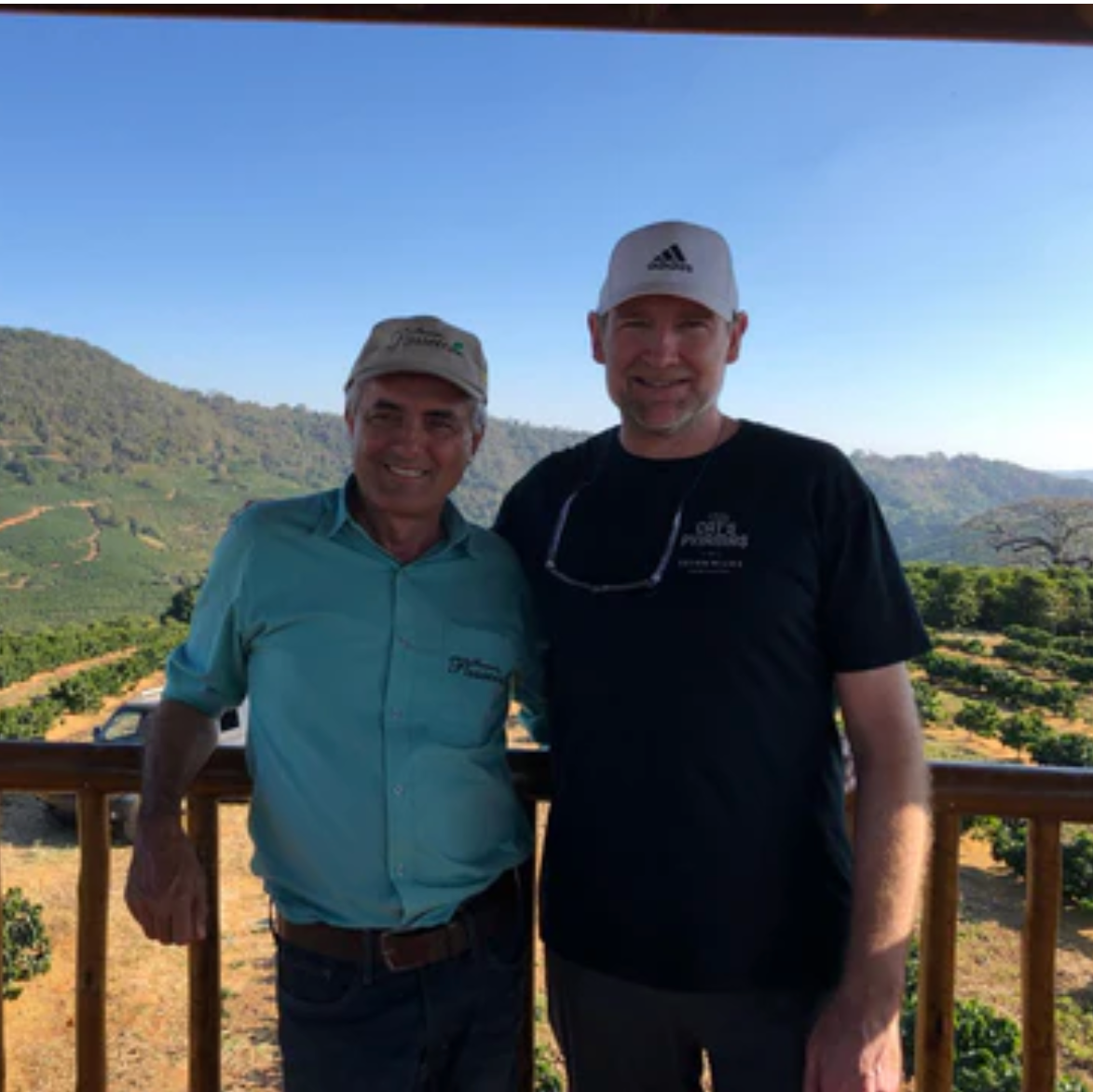 Two men standing on a balcony with a scenic view of green fields and hills.