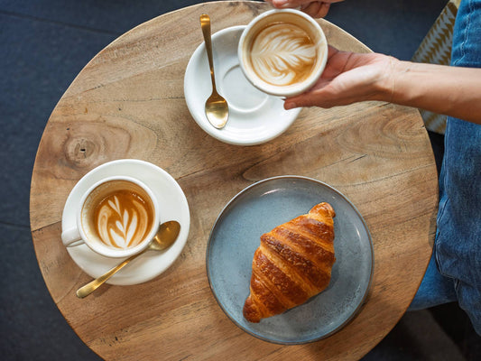 top down shot of coffees and a croissant on a table in a cafe