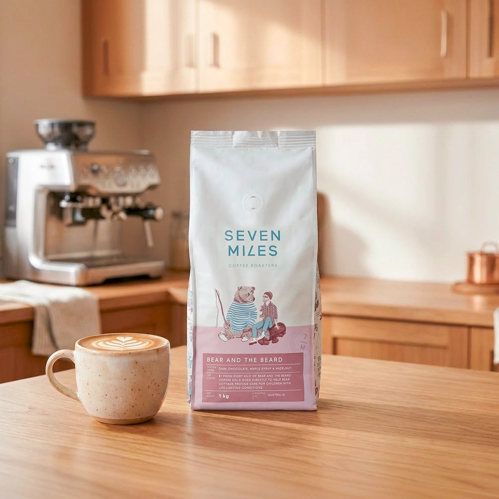 Seven Miles Coffee Bear and the Beard 1kg bag featuring dark chocolate, maple and hazelnut notes, styled with latte art in modern kitchen.