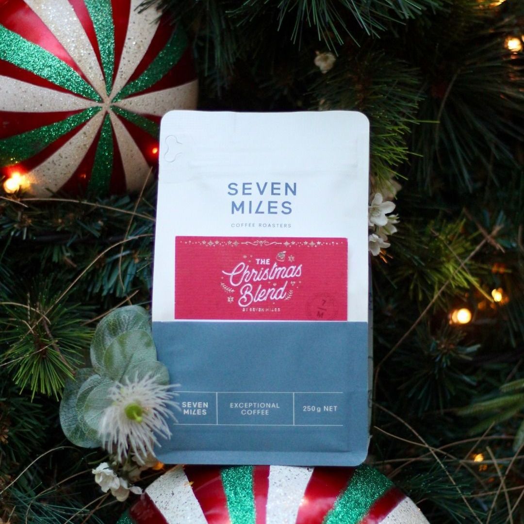 even Miles Christmas Blend coffee package surrounded by festive holiday decorations, premium seasonal coffee from Seven Miles Coffee Roasters.